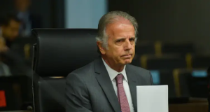 O ministro da Defesa, José Múcio, segurando papel, com expressão brava, olhando "de rabo de olho"