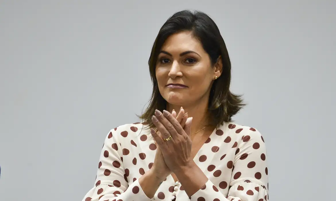 Michelle Bolsonaro de cabelo solto e roupa clara, batendo palmas