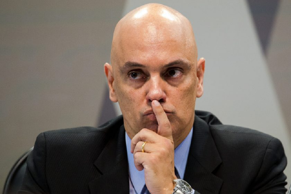 ministro Alexandre de Moraes olhando para o lado, com a mão na boca, sério