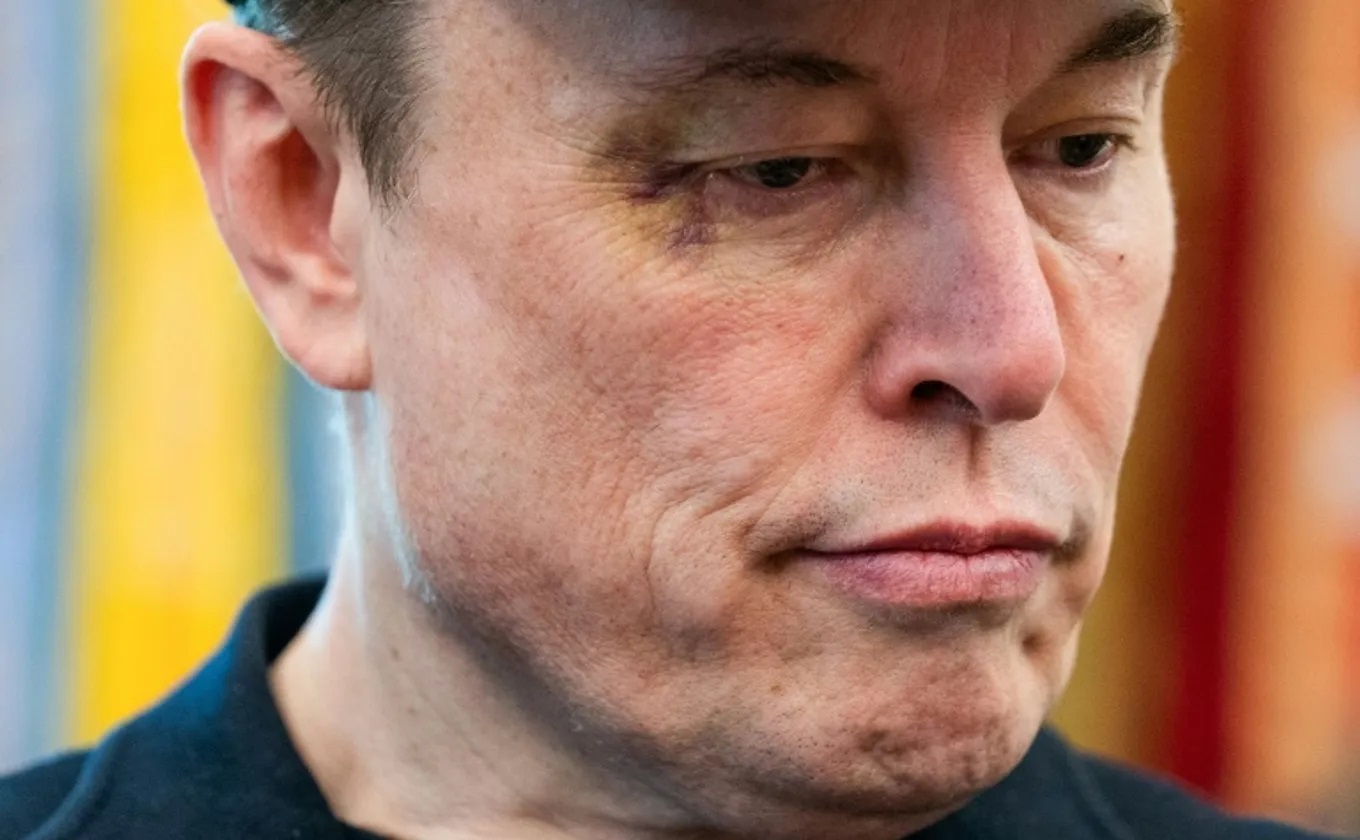 Elon Musk sério, com olho roxo, em close, sem olhar para a câmera