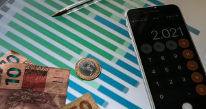 Cédulas e moedas de reais e calculadora aberta em tela de celular