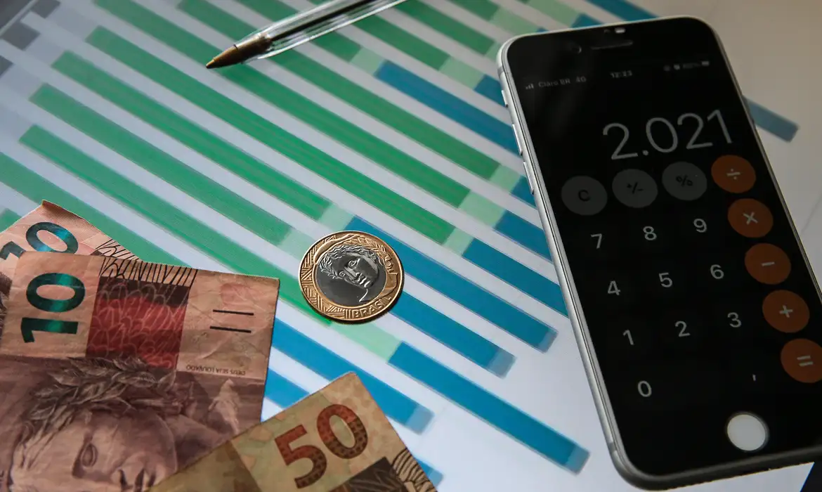Cédulas e moedas de reais e calculadora aberta em tela de celular
