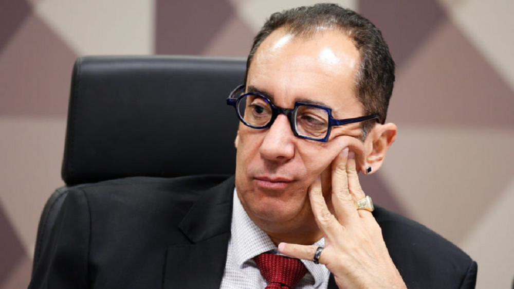 senador Jorge Kajuru (PSB-GO) de óculos, olhando para o lado, com o rosto apoiado em uma das mãos e sério