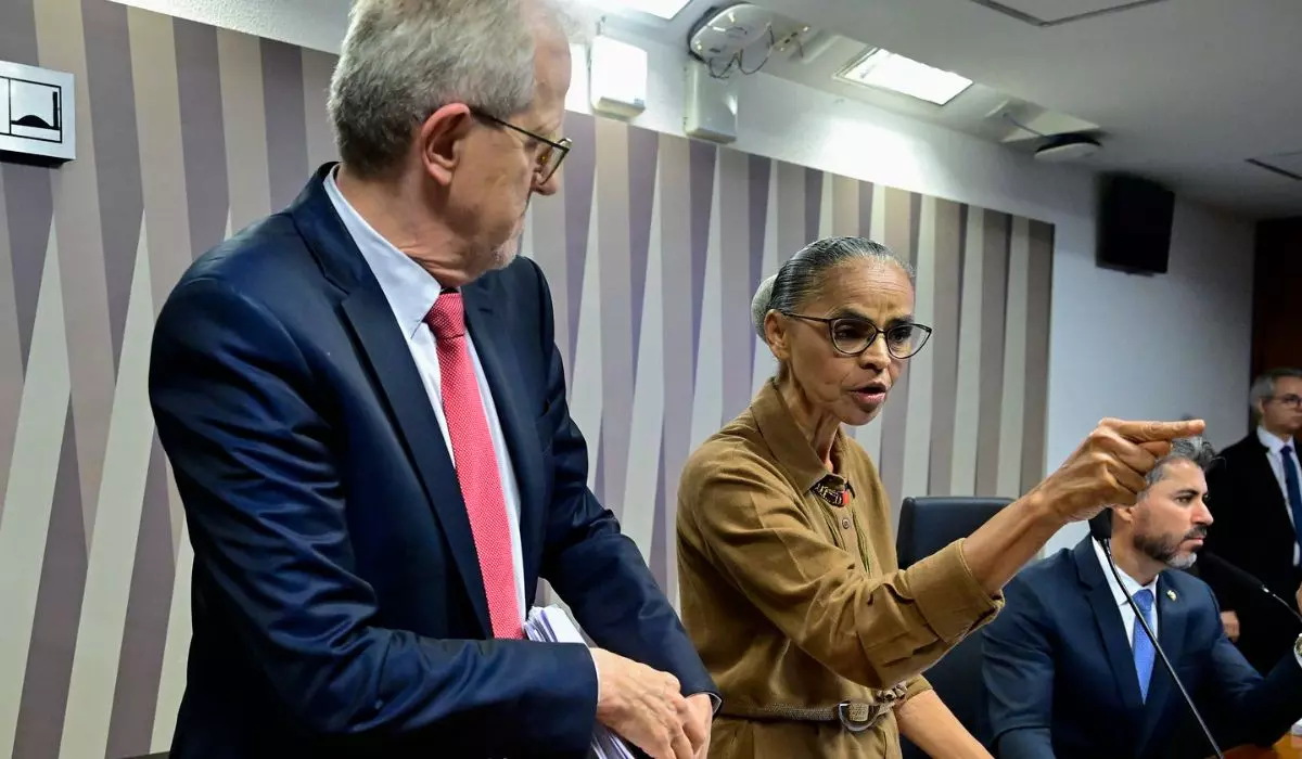 ministra do Meio Ambiente e Mudanças Climáticas, Marina Silva, de roupa bege e cabelo preso, em pé, apontando e falando, sem olhar para a câmera