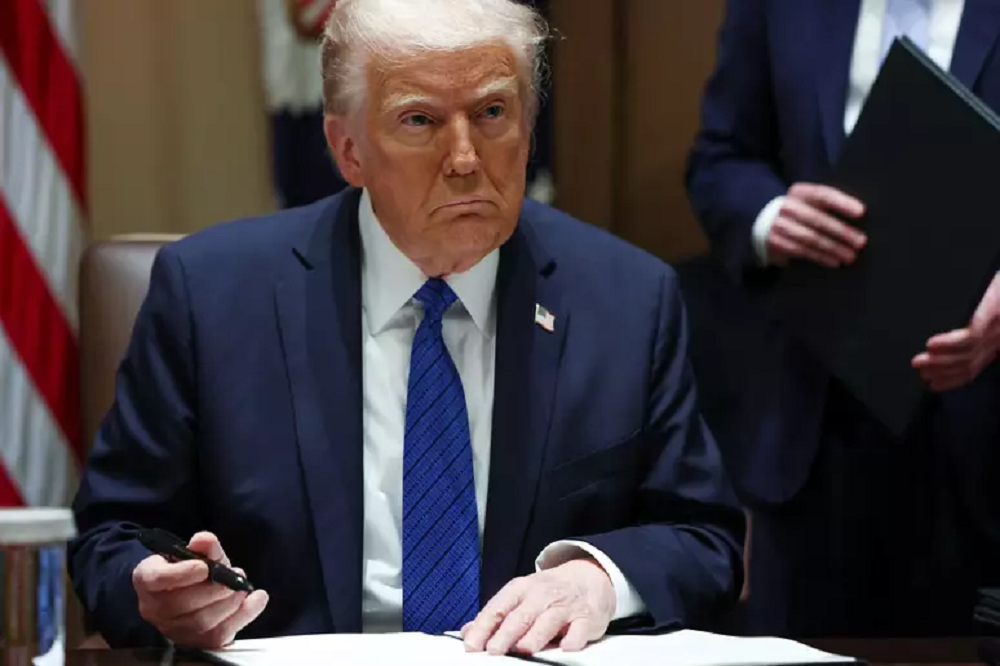 Donald Trump assinando papel com expressão triste