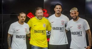 Quatro homens lado a lado com camisetas do Corinthians com anúncio da Vai de Bet