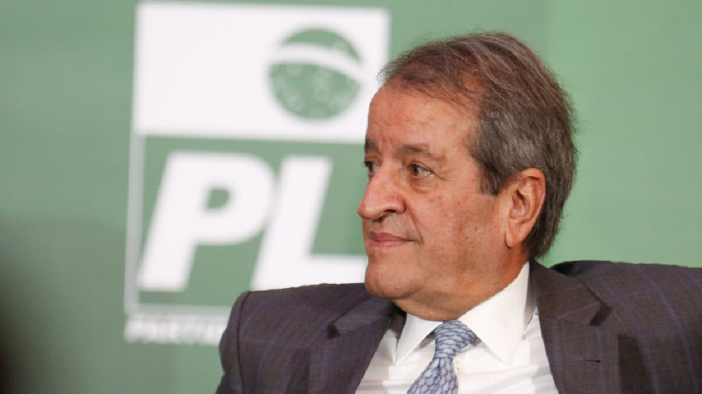 Valdemar Costa Neto olhando para o lado esquerdo da foto, com símbolo do PL ao fundo