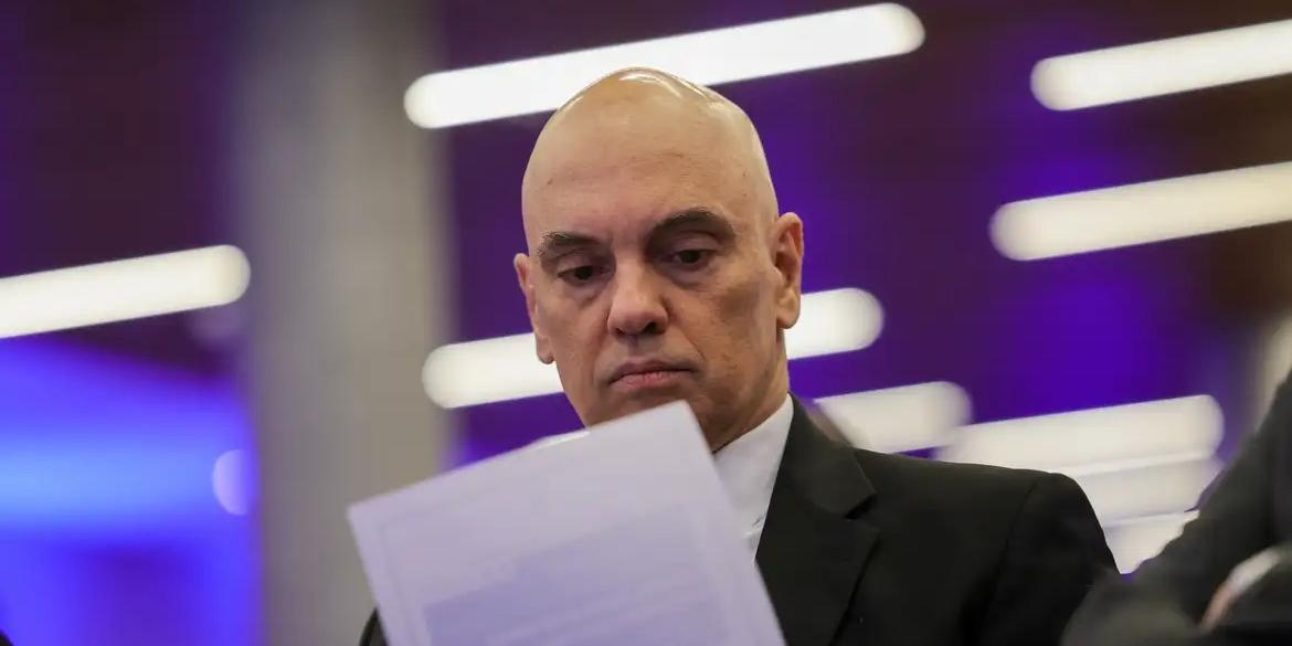 ministro Alexandre de Moraes sério, olhando pra baixo, lendo papel