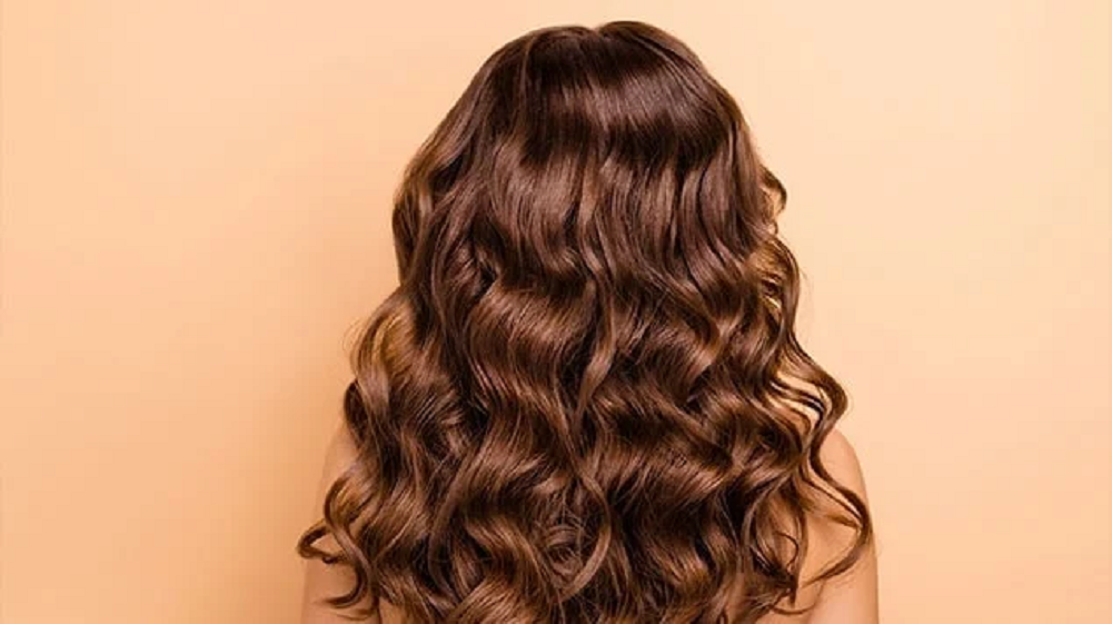 Mulher de costas com cabelo castanho e ondulado aparecendo
