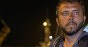 ativista Thiago Ávila no canto esquerdo de foto, sério, sem olhar para a câmera, em close