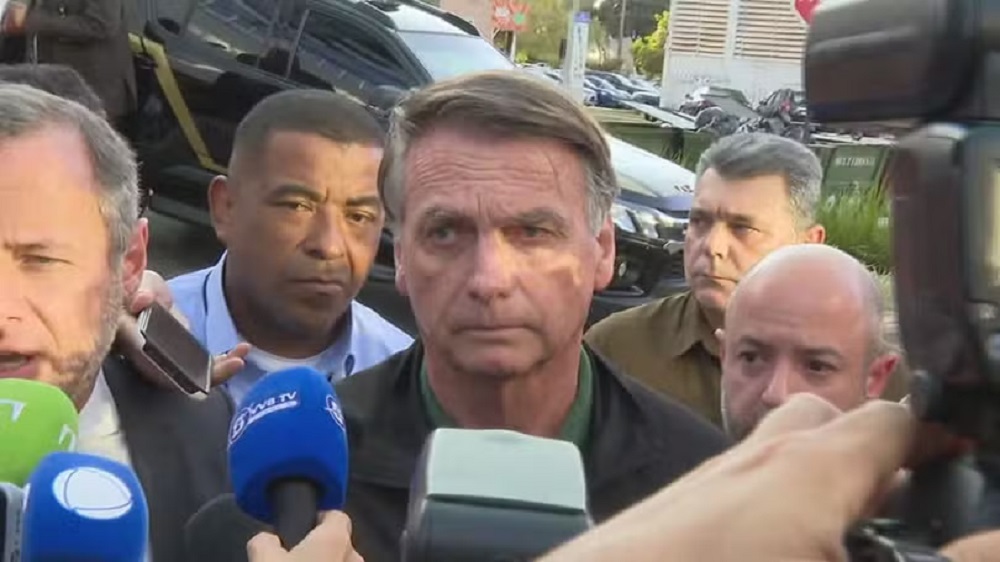 Jair Bolsonaro com expressão séria, sem olhar para a câmera, cercado de pessoas