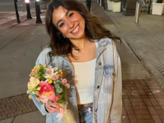 brasileira Caroline Dias Gonçalves sorrindo para a câmera, segurando flores, de roupa branca e jeans