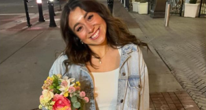 brasileira Caroline Dias Gonçalves sorrindo para a câmera, segurando flores, de roupa branca e jeans
