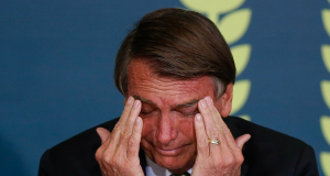 Jair Bolsonaro (PL) cabisbaixo, com as mãos no rosto e cara de choro