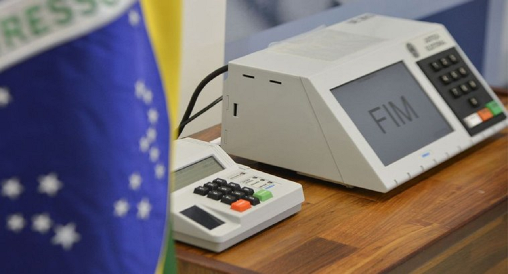 Urna eletrônica com uma bandeira do Brasil ao lado