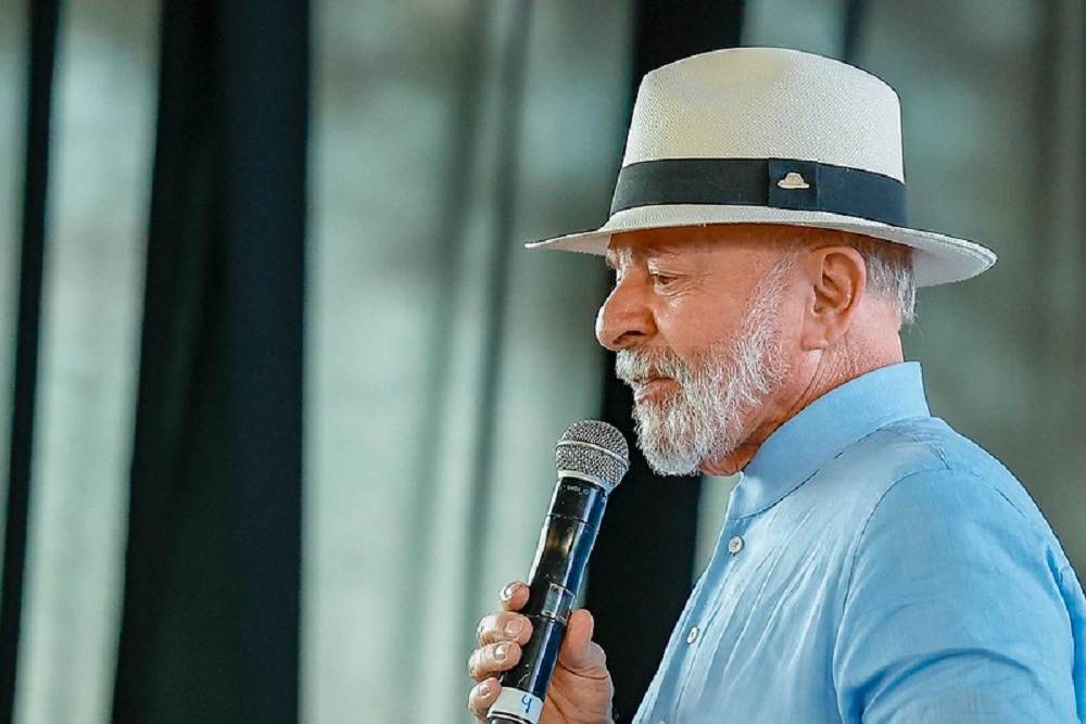 Lula de camisa azul e chapéu, de perfil, falando em microfone