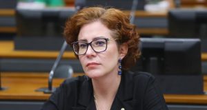 A deputada licenciada Carla Zambelli (PL-SP) séria, de óculos, roupa preta e cabelo solto, sem olhar para a câmera
