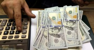 Mão com calculadora ao lado de cédulas de dólar