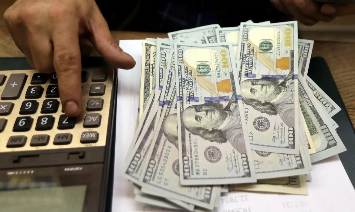 Mão com calculadora ao lado de cédulas de dólar