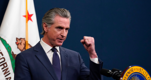 O governador da Califórnia, Gavin Newsom, falando em microfone, sério