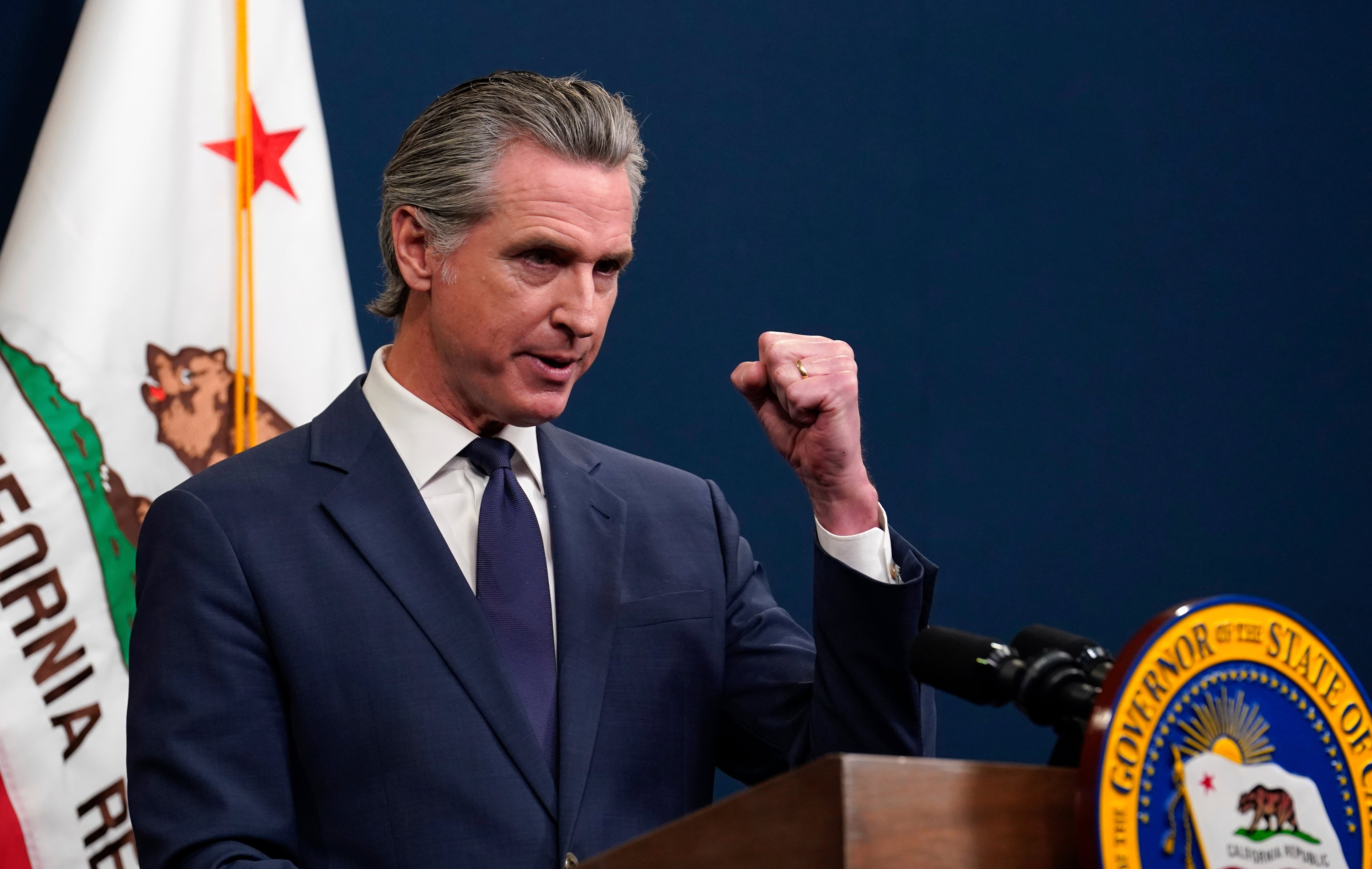 O governador da Califórnia, Gavin Newsom, falando em microfone, sério
