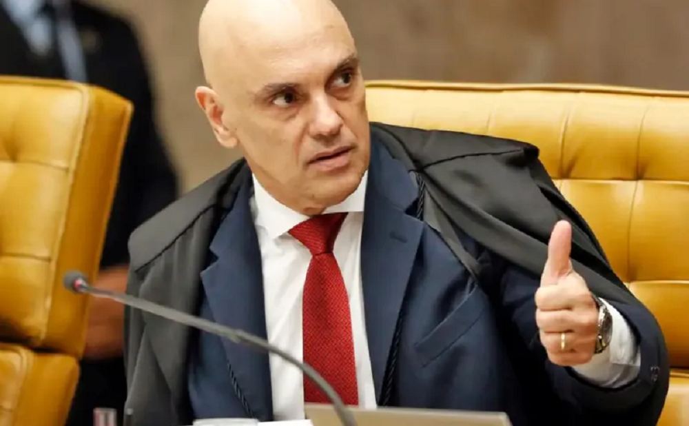 ministro Alexandre de Moraes, do STF fazendo sinal de joia, olhando para o lado, sério