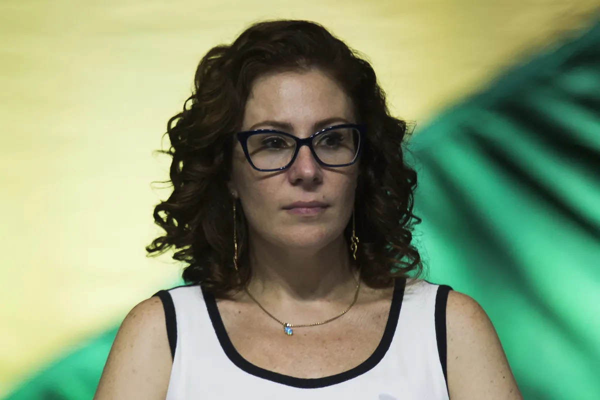 deputada federal Carla Zambelli com expressão triste, de camiseta branca e preta e óculos, sem olhar para a câmera