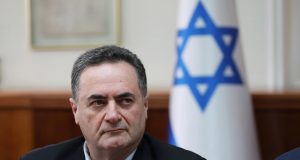 Ministro da Defesa, Israel Katz, sério, olhando para o lado esquerdo, com bandeira de Israel ao fundo