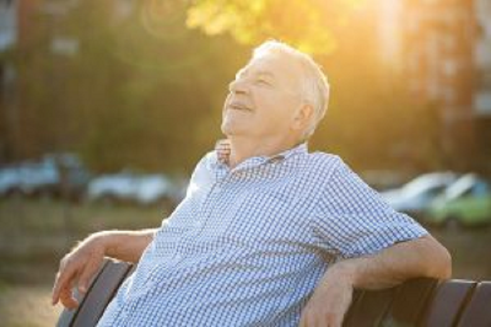 Idoso se expondo ao sol, sorrindo, sentado