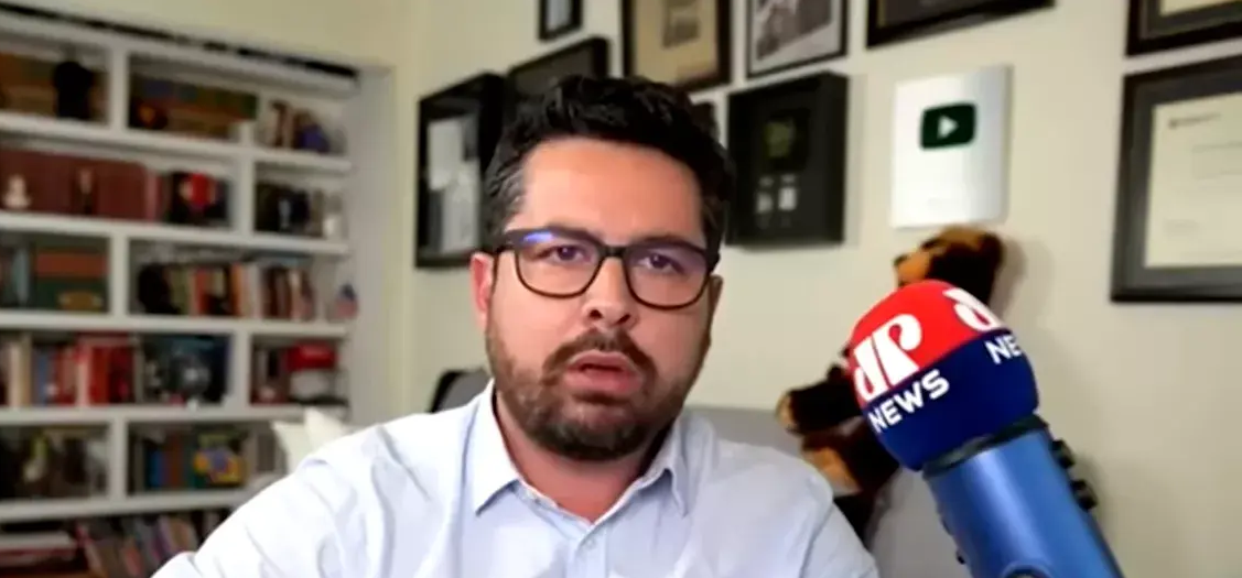 Paulo Figueiredo de óculos e roupa branca, com expressão de espanto, perto de microfone da Jovem Pan News