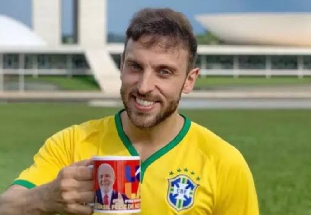 Léo Lins sorrindo com camisa do Brasil e caneca do Lula na Praça dos Três Poderes