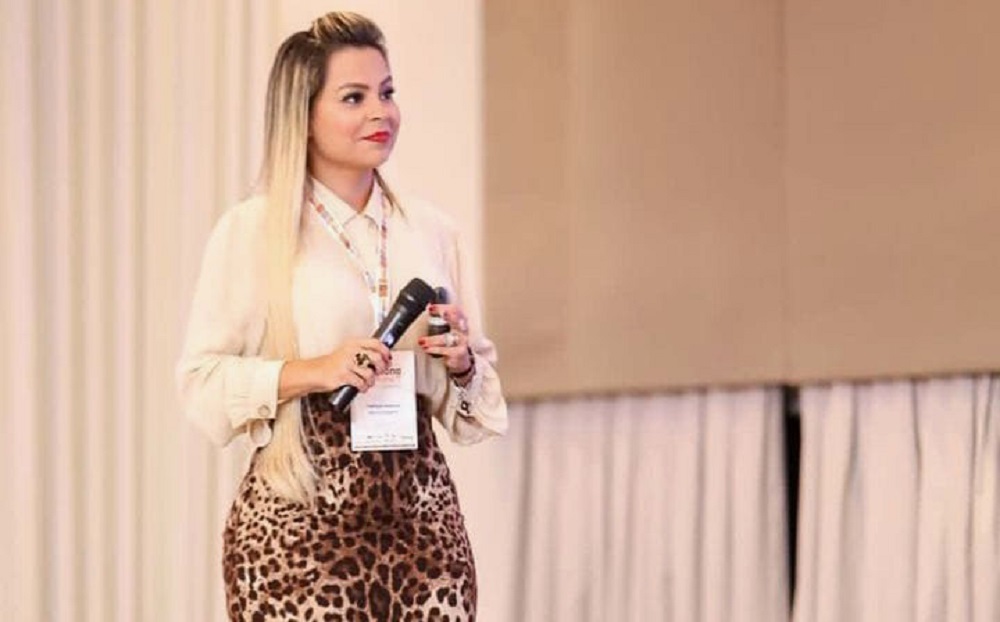prefeita de Marituba (PA), Patrícia Alencar (MDB), em pé, de saia de oncinha e camisa branca, de cabelo solto, segurando microfone, sem olhar para a câmera, no canto esquerdo de foto