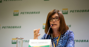 A presidente da Petrobras, Magda Chambriard, falando em microfone e gesticulando, de roupa azul e cabelo solto