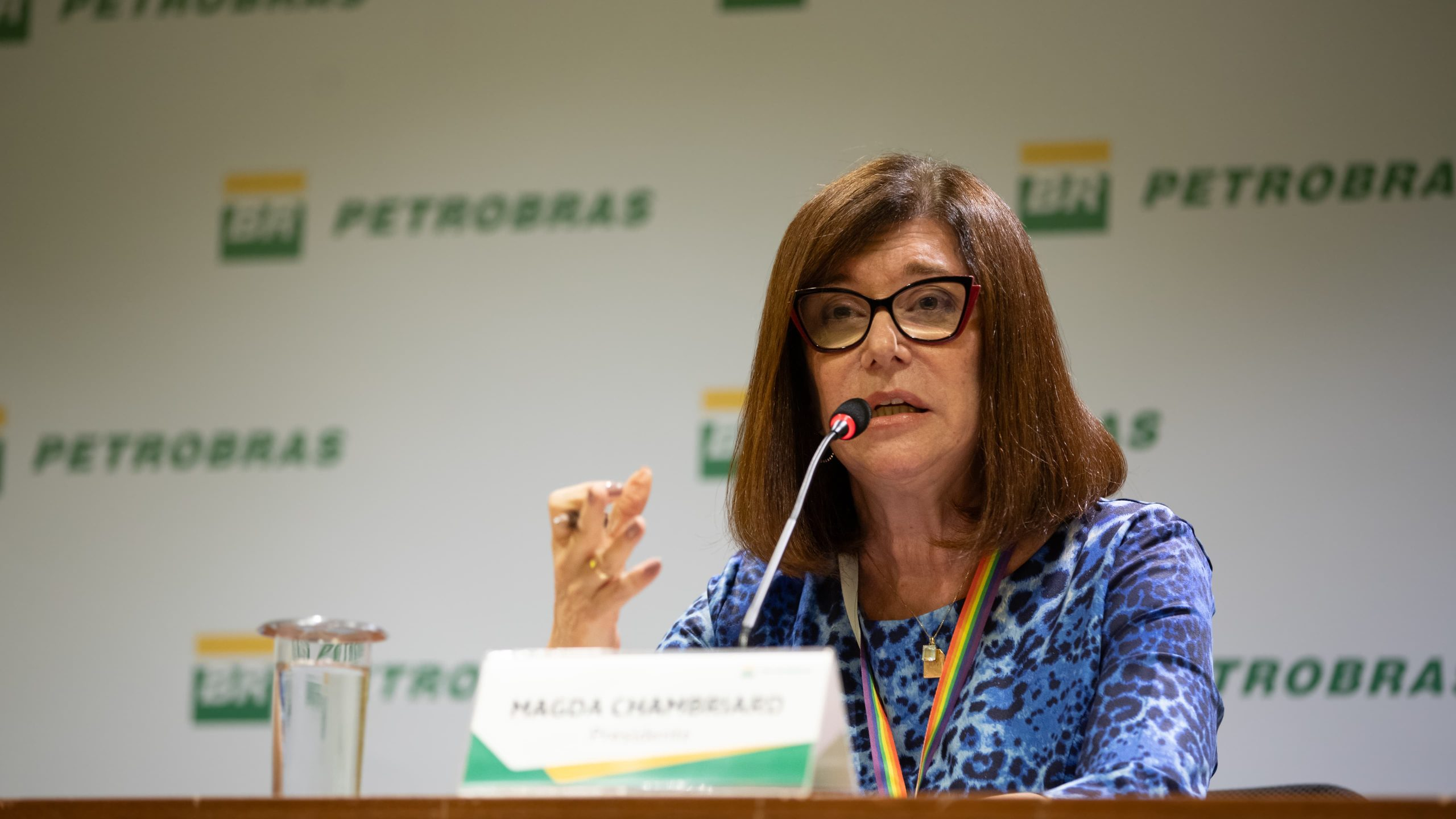 A presidente da Petrobras, Magda Chambriard, falando em microfone e gesticulando, de roupa azul e cabelo solto