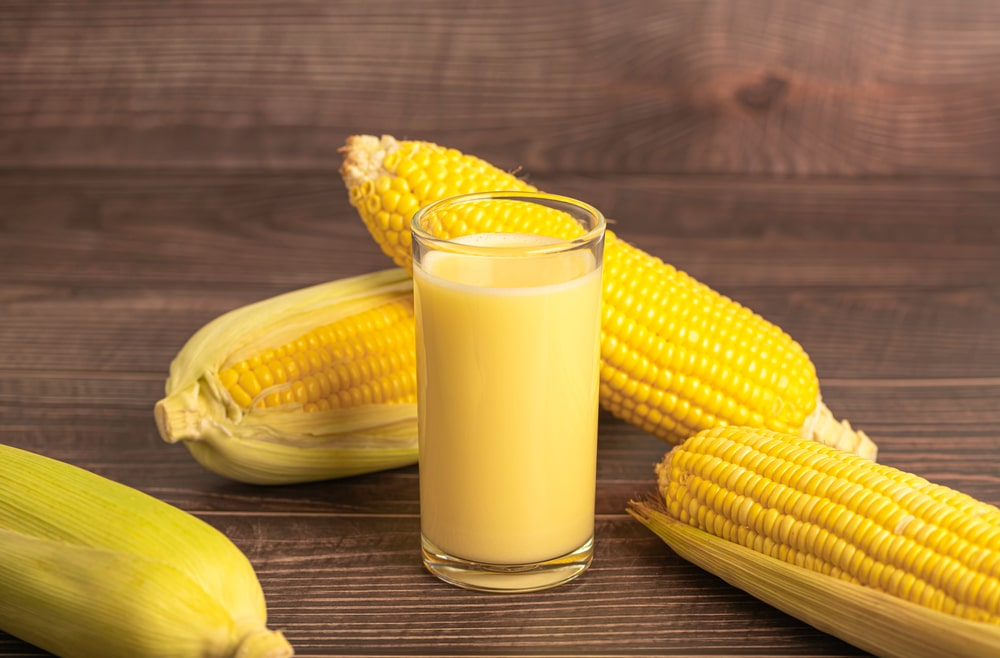 Suco de milho em copo de vidro e espigas de milho