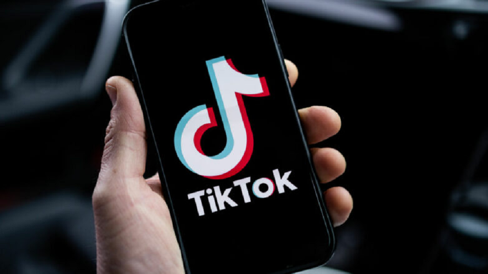 Mão segurando celular com logo do TikTok