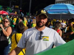Manoel Abílio Pacífico, militante de extrema-direita, de boné, segurando bandeira com a foto de Bolsonaro
