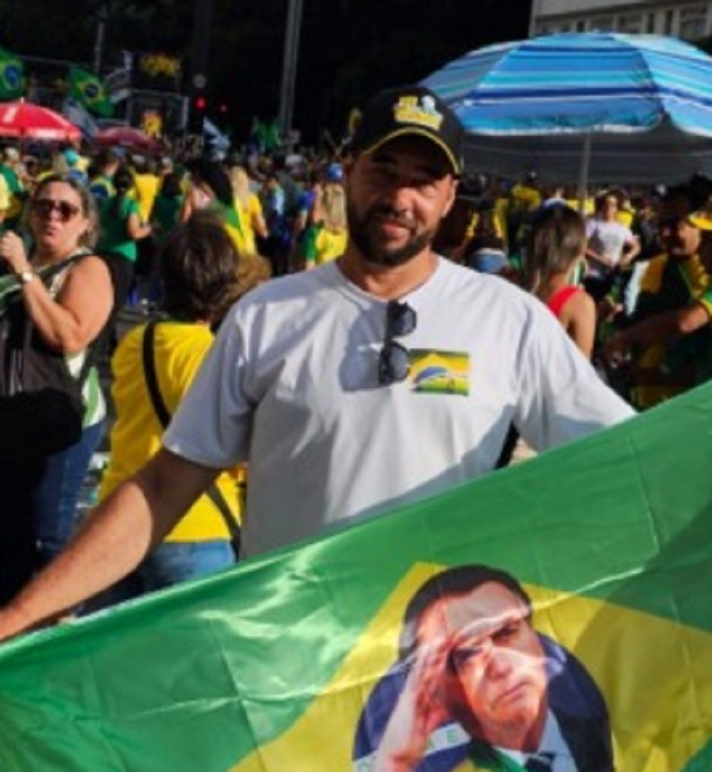 Manoel Abílio Pacífico, militante de extrema-direita, de boné, segurando bandeira com a foto de Bolsonaro