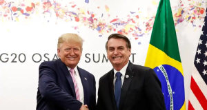 Donald Trump e Jair Bolsonaro em aperto de mãos, sorrindo para a câmera