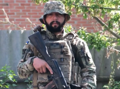 O brasileiro Rafael Paixão fardado, segurando arma, olhando sério para a câmera