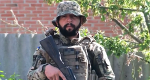 O brasileiro Rafael Paixão fardado, segurando arma, olhando sério para a câmera