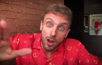O humorista Léo Lins de roupa vermelha com cara de espanto, olhando pra câmera