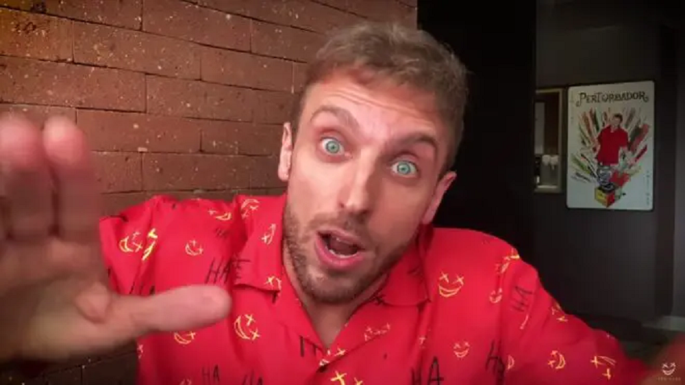 O humorista Léo Lins de roupa vermelha com cara de espanto, olhando pra câmera