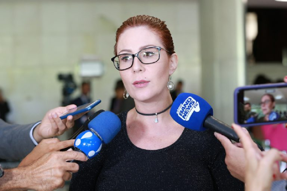 deputada federal licenciada Carla Zambelli (PL-SP) falando em microfones, séria, de óculos e cabelo preso