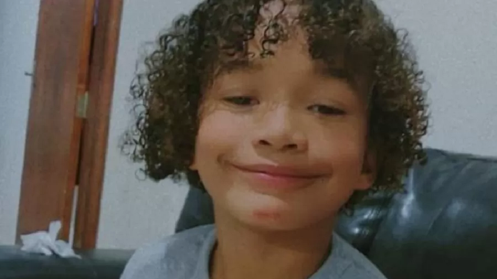 Noah Miguel dos Santos sorrindo para a câmera, em close, de camiseta cinza