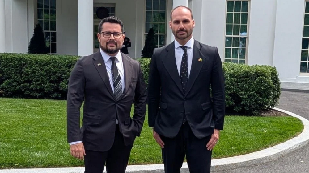 O jornalista Paulo Figueiredo e o deputado federal licenciado Eduardo Bolsonaro (PL) em pé lado a lado, olhando para a câmera