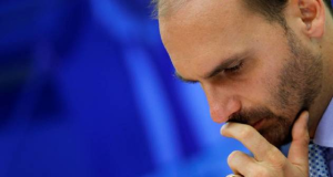 deputado federal licenciado Eduardo Bolsonaro (PL-SP) no canto direito da foto, cabisbaixo, sério, com uma mão na boca