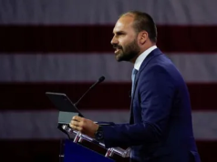 O deputado federal licenciado Eduardo Bolsonaro (PL) em pé, falando em microfone