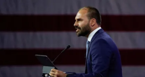 O deputado federal licenciado Eduardo Bolsonaro (PL) em pé, falando em microfone