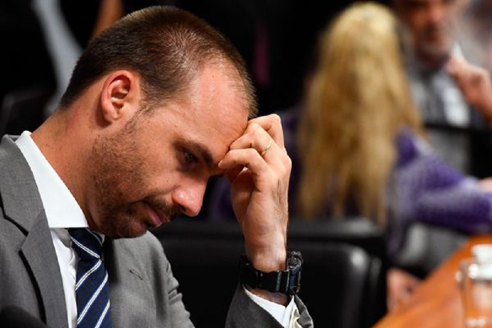 Eduardo Bolsonaro (PL-SP) de perfil, em close, cabisbaixo, com a mão no rosto